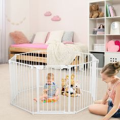 a woman sitting on the floor next to a baby in a playpen with stuffed animals