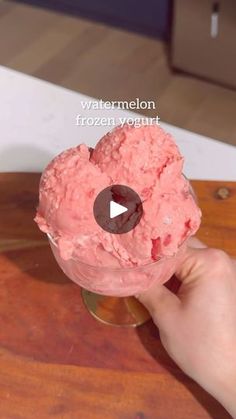 a person is holding up a pink ice cream in a glass with a video playing on it