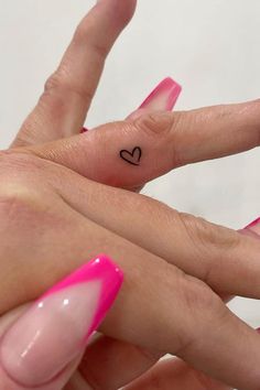 two hands with pink fingernails and one has a small heart tattoo on the middle finger