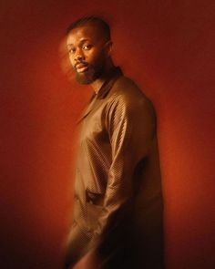 a man standing in front of a red wall with his hands on his hips and looking at the camera