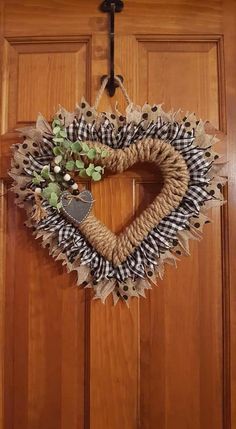 a heart shaped wreath hanging on the front door with burlocks and greenery