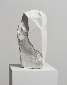 a white sculpture sitting on top of a block of paper in front of a gray wall