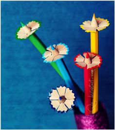 three pencils with flowers on them in front of a blue background and the bottom one is made out of colored crayons