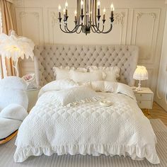 a bed with white comforter and pillows in a bedroom next to a chandelier