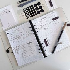 an open planner and pen on top of a white table next to other office supplies