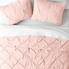 a bed with pink sheets and pillows on top of it, next to a white headboard