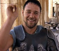 a man in armor is smiling and raising his fist up to the camera while sitting on a bench