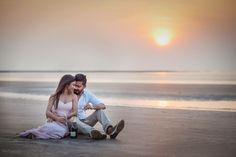 a man and woman are sitting on the beach at sunset with bottles in their hands