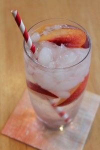 a glass filled with ice and fruit sitting on top of a wooden table next to a red and white striped straw