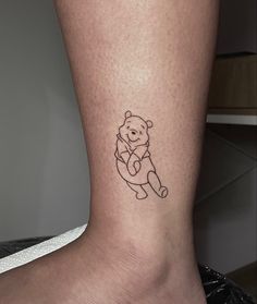 a small tattoo of a teddy bear on the ankle is shown in black ink,