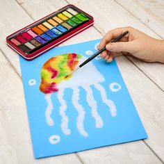 a child's hand holding a paintbrush over a paper with a jellyfish on it