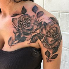 a woman's shoulder with roses and leaves on her left arm, in front of a white brick wall