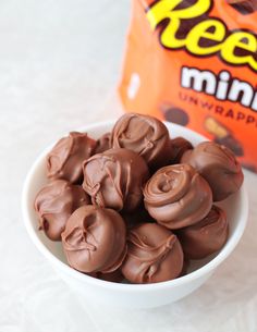 a white bowl filled with chocolate candy next to a bag of reeses