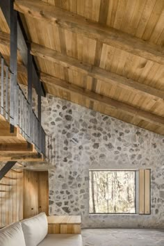 a living room with stone walls and wooden ceilings, along with a staircase leading up to the second floor