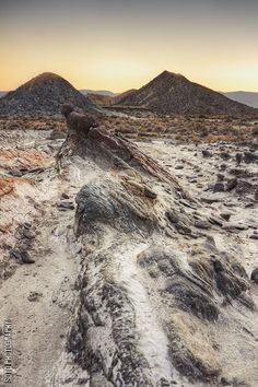 the sun is setting over some mountains in the desert with rocks and dirt on it