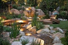 a garden with rocks and water features lit up by lights in the center, surrounded by greenery