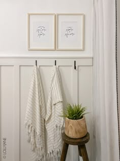 two towels hanging on the wall next to a potted plant and a wooden stool