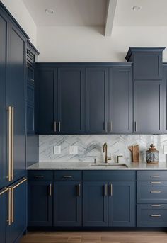 a kitchen with dark blue cabinets and marble counter tops, gold pulls on the handles