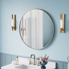 a bathroom with blue walls and white counter tops, gold fixtures and a round mirror above the sink