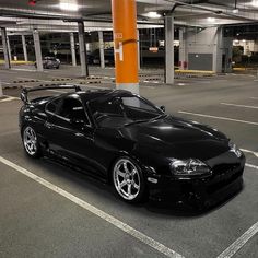 a black sports car parked in a parking lot next to an orange pole with lights on