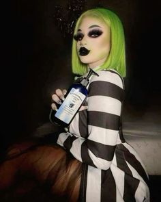 a woman with green hair and makeup holding a bottle