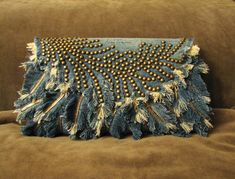 a blue purse with gold beading on it sitting on top of a brown couch