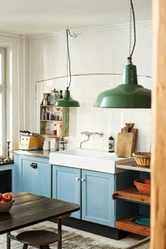 a kitchen with blue cabinets and green lights hanging from the ceiling, along with an old fashioned coffee table