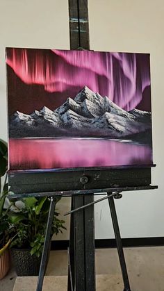 an easel with a painting on it in front of a potted plant