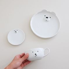 a hand is holding a white cup with a bear face on it and another one has a plate in the shape of a polar bear