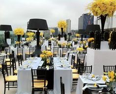 an outdoor dining area with tables and chairs covered in white tablecloths, yellow flowers and black lampshades