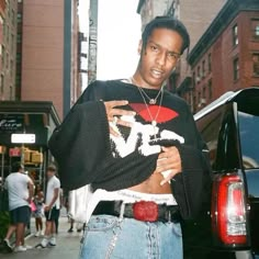 a man standing in front of a car on the street wearing a sweater and jeans