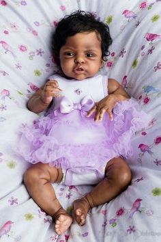 a baby in a purple dress laying on a bed