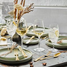 the table is set with wine glasses, silverware and gold utensils on it