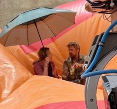 a man and woman sitting in an inflatable tent with umbrellas over their heads