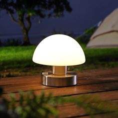 a lamp sitting on top of a wooden table next to a tent in the background