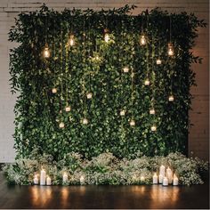 candles are lit in front of a wall covered with greenery and hanging mason jars