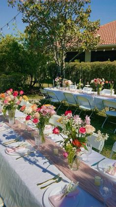 an outdoor table set up with flowers and place settings for guests to sit down at