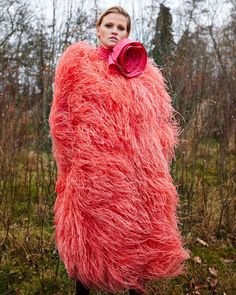 a woman is standing in the grass with a large pink coat on her shoulders and hands behind her back