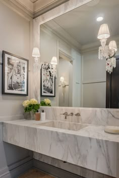 a bathroom with marble counter top and white sink under a chandelier hanging from the ceiling