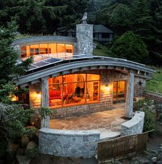 a house that is surrounded by trees and rocks with lights on the windows at night