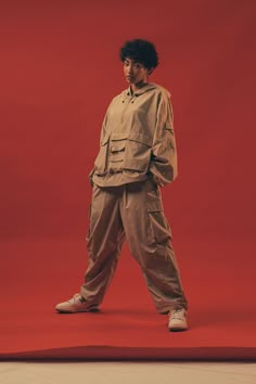 a man standing in front of a red background wearing an orange shirt and khaki pants