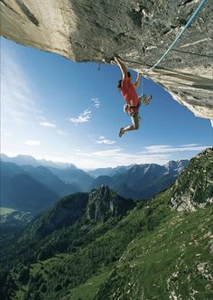 a man climbing up the side of a mountain with his hands in the air while holding onto a rope