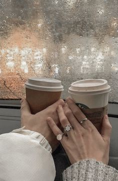 two people holding coffee cups in their hands while looking out the window on a rainy day