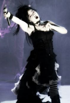 a woman dressed in black and white holding a knife with her right arm out while performing on stage