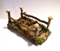 a miniature house made out of wood and moss with mushrooms on the roof, sitting on a white surface