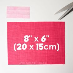 a piece of pink fabric with the measurements printed on it and two pairs of scissors next to it