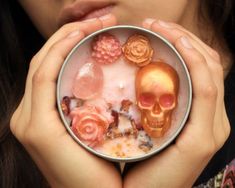 a woman holding a metal container with fake flowers and skulls in it's center