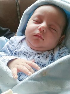 a baby sleeping in a blue blanket on top of a couch with his eyes closed