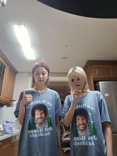 two people wearing t - shirts with faces drawn on them in the middle of a kitchen