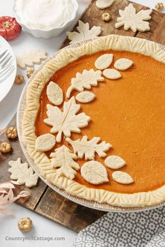 a pumpkin pie with leaves on top and other fall decorations around the edges, sitting on a cutting board